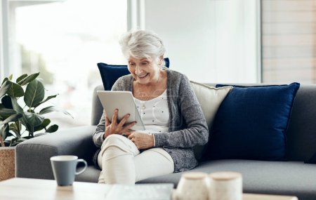 Foto de Una buena risa es la mejor cura para cualquier cosa. una mujer mayor usando una tableta digital mientras se relaja en casa - Imagen libre de derechos