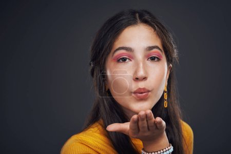 Photo for Sending you good energy. Cropped portrait of an attractive teenage girl standing alone and blowing kisses against a dark studio background - Royalty Free Image