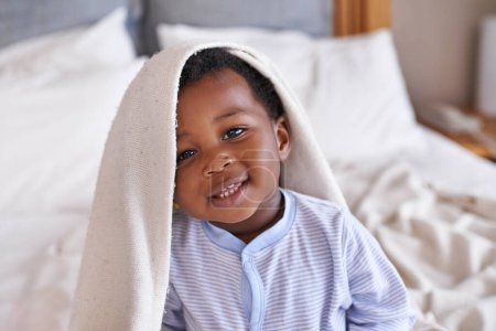 Téléchargez les photos : Portrait, heureux et bébé avec une couverture au lit, se réveiller et jouer dans sa maison. Visage, sourire et tout-petit garçon africain dans une chambre curieuse, amusante et douce, mignonne et ludique tout en se relaxant. - en image libre de droit