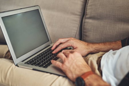 Photo for Blogging is a lifestyle. an unrecognizable man using his laptop while relaxing on a couch at home - Royalty Free Image