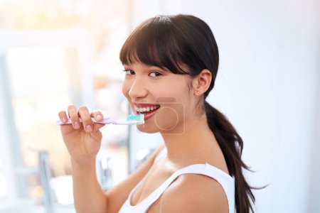Téléchargez les photos : Juste un peu de brossage. Portrait d'une jeune femme séduisante et joyeuse se brossant les dents à la maison pendant la journée - en image libre de droit
