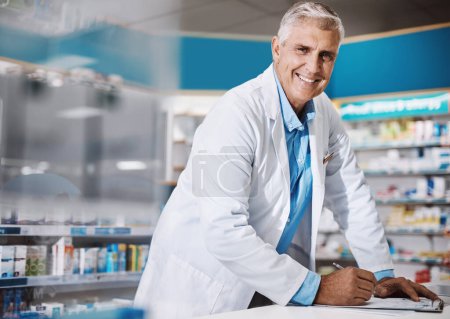 Foto de Estoy al servicio de mejorar vidas. un farmacéutico masculino que escribe en un portapapeles en una farmacia - Imagen libre de derechos