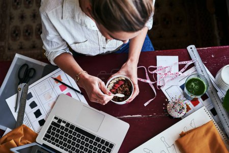 Foto de No podré trabajar con el estómago vacío. una diseñadora de moda desayunando mientras trabaja en su escritorio - Imagen libre de derechos