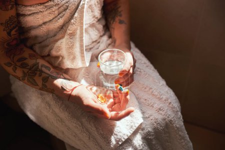 Téléchargez les photos : Ce n'est pas le matin sans multivitamine. une femme prenant une pilule avec un verre d'eau pendant sa routine matinale à la maison - en image libre de droit