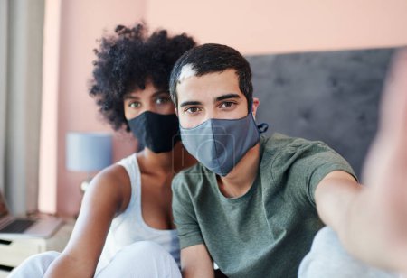Foto de Mantén la calma y usa tu mascarilla. una pareja joven tomando una selfie mientras usa sus máscaras - Imagen libre de derechos