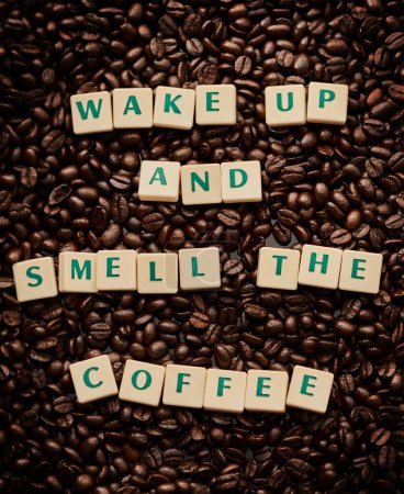Téléchargez les photos : Laissez le café éveiller vos sens. Gros plan de lettres formant les mots se réveillent et sentent le café sur une pile de grains de café - en image libre de droit
