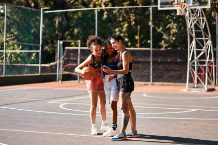 Foto de ¿Qué está pasando aquí? un grupo diverso de deportistas de pie juntos después de jugar baloncesto y mirando un teléfono celular - Imagen libre de derechos