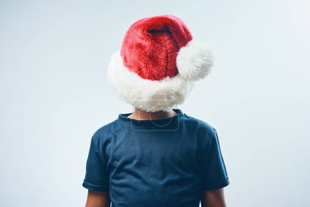 Foto de ¿Alguien ha visto mi sombrero? Estudio de un lindo niño cubriéndose la cabeza con un sombrero de Santa Claus sobre un fondo gris - Imagen libre de derechos