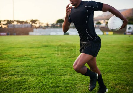 Photo for Working on my speed. an unrecognizable sportsman running alone while holding a rugby ball during an early morning practice - Royalty Free Image
