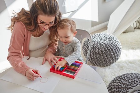 Foto de Aprender sobre formas y colores. una mujer y su hijo pequeño usando lápices de colores para dibujar en casa - Imagen libre de derechos