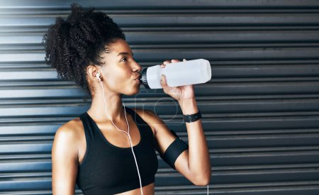 Foto de La hidratación es particularmente importante para el entusiasta del entrenamiento. una joven deportista bebiendo agua mientras hace ejercicio sobre un fondo gris - Imagen libre de derechos