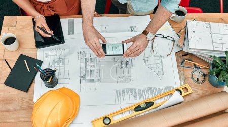 Photo for Its so simple to save and share their ideas. Closeup shot of two unrecognisable architects using a cellphone to take photos of blueprints in an office - Royalty Free Image