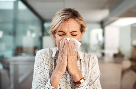 Foto de Podría ser la gripe. una mujer de negocios madura sonándose la nariz mientras trabaja en una oficina - Imagen libre de derechos