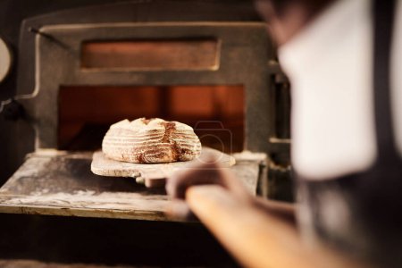 Foto de Recién salido del horno. un panadero macho que retira el pan recién horneado del horno - Imagen libre de derechos