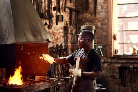 Foto de El hierro afila el hierro. un joven trabajador de metal guapo afilando una varilla de metal caliente dentro de un taller de soldadura - Imagen libre de derechos