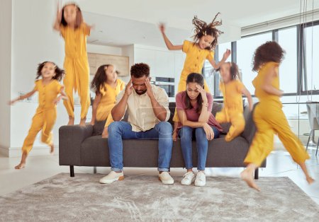 Photo for Stressed mixed race parents and adhd daughter in living room at home. Hyperactive hispanic girl running and jumping around lounge. Mother and father sitting together with headache and feeling anxious. - Royalty Free Image
