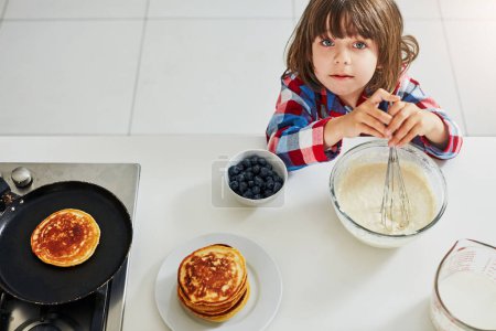 Téléchargez les photos : Je prépare le petit déjeuner aujourd'hui. Plan grand angle d'un adorable petit garçon faisant des crêpes dans la cuisine à la maison - en image libre de droit