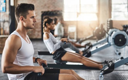 Foto de Concéntrate, mantente en forma. un joven haciendo ejercicio con una máquina de remo en el gimnasio - Imagen libre de derechos