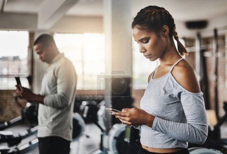 Foto de Fitness facilitado con aplicaciones inteligentes. una joven usando un teléfono móvil en un gimnasio - Imagen libre de derechos