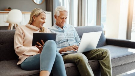 Foto de Esto es lo que sucede cuando ahorras para la jubilación. una pareja madura usando una tableta digital y un portátil en el sofá en casa - Imagen libre de derechos
