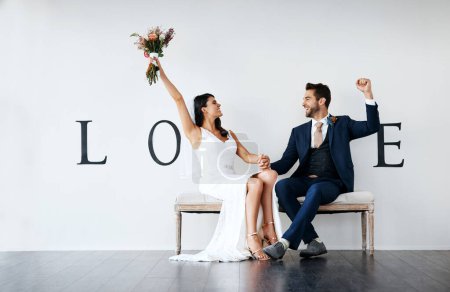 Photo for We got hitched. Concept studio shot of a bride and groom making an V in the word love against a wall - Royalty Free Image