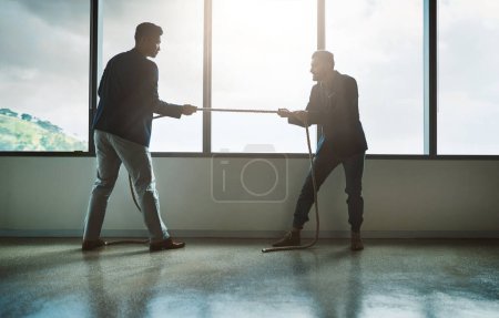 Photo for No one pushes you to achieve more than your competitor. two young businessmen pulling on a rope in a game of tug of war - Royalty Free Image