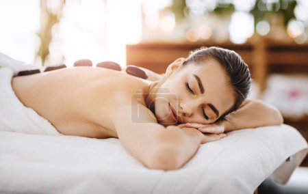 Foto de Voy a cerrar los ojos mientras lo tomo. una mujer joven recibiendo terapia de piedra caliente en un spa - Imagen libre de derechos