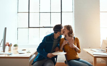 Téléchargez les photos : Plus qu'une romance de bureau. jeune couple embrasser tout en travaillant ensemble dans leur bureau moderne - en image libre de droit