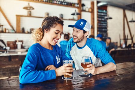 Téléchargez les photos : Donc, vous êtes un fan de sport aussi. un jeune homme et une jeune femme qui boivent des bières en regardant un match de sport dans un bar - en image libre de droit