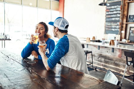 Téléchargez les photos : Le couple qui regarde le sport ensemble. un jeune homme et une jeune femme qui boivent des bières en regardant un match de sport dans un bar - en image libre de droit