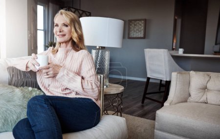 Téléchargez les photos : Buvez du thé et soyez juste. une femme mûre se relaxant sur le canapé à la maison avec une tasse de café - en image libre de droit
