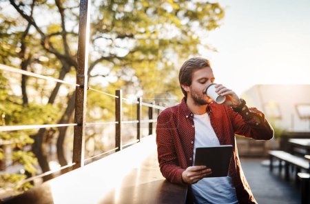 Foto de Café y conectividad. un joven guapo usando su tableta digital mientras bebe café afuera - Imagen libre de derechos