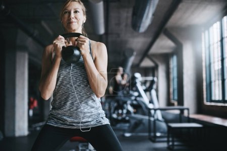 Photo for Being a lifter gets her fitter. an attractive young woman listening to music while working out with a kettle bell in the gym - Royalty Free Image