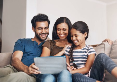Téléchargez les photos : Comment les familles modernes se connectent. une mère et un père utilisant une tablette numérique avec leur fille sur le canapé à la maison - en image libre de droit