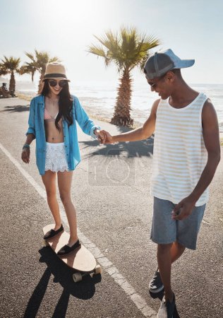 Téléchargez les photos : Je suis juste là. un jeune homme enseignant à sa petite amie comment skater sur la promenade - en image libre de droit