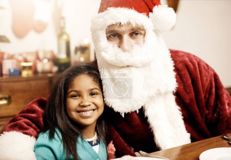 Foto de Adivina quién vino a comer en Navidad. Retrato de una adorable niña disfrutando de la Navidad con su padre disfrazado de Papá Noel en casa - Imagen libre de derechos