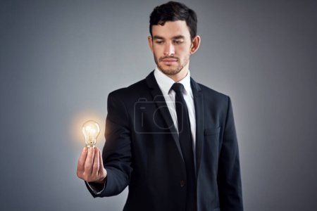Foto de Nada evoluciona el negocio como la innovación. Estudio de un joven hombre de negocios sosteniendo una bombilla brillante sobre un fondo gris - Imagen libre de derechos