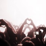 Hands, heart and phone in the audience with people watching a concert or music festival event. Party, dance or disco with a group of men and women in the crowd while attending a stage performance.