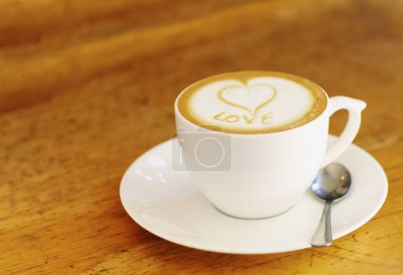 Foto de Café, café con leche y mesa de madera en la cafetería vintage con una taza en un restaurante con un fondo liso. Expresso, cocina y bebida con leche y espuma en el restaurante retro para el desayuno por la mañana con amor. - Imagen libre de derechos