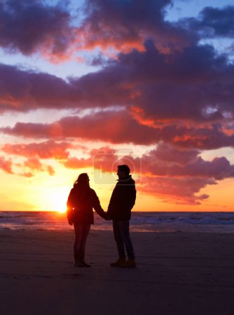 Téléchargez les photos : Couple, silhouette et coucher de soleil sur la plage à un rendez-vous romantique, vacances ou vacances dans la nature. Homme et femme tenant la main avec amour et soin sur le voyage, l'aventure ou le voyage avec les nuages et l'océan. - en image libre de droit
