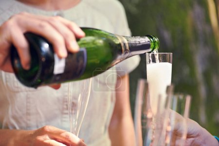 Photo for Hand, pour champagne and glasses for group of friends for celebration, toast and party in park, garden or nature. Bottle, sparkling wine and glass to celebrate for team of people, birthday or event. - Royalty Free Image