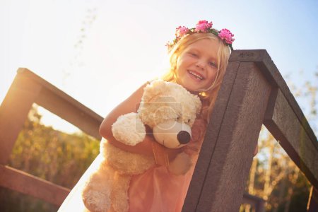 Foto de Ella tiene un gran día con el mejor amigo. una niña feliz sosteniendo un oso de peluche y mirando a la cámara mientras está de pie en un puente - Imagen libre de derechos