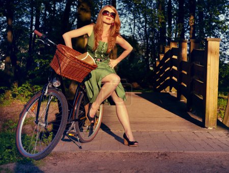 Téléchargez les photos : Style, pont et vélo avec femme dans le parc pour le vélo, la tendance et la nature. Joyeux, sourire et mode avec cycliste vintage et vélo reposant à la campagne pour la santé, vacances d'été ou élégant. - en image libre de droit