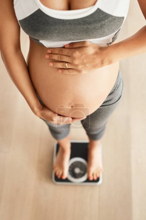 Foto de Cuánto he crecido. Cortado tiro de ángulo alto de una mujer embarazada pesándose en una balanza - Imagen libre de derechos