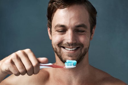 Foto de Tengo que mantener esa sonrisa brillante. un joven guapo cepillándose los dientes sobre un fondo gris - Imagen libre de derechos