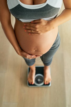 Foto de Controlar el aumento de peso saludable durante el embarazo con pesas diarias. Cortado tiro de ángulo alto de una mujer embarazada pesándose en una balanza - Imagen libre de derechos