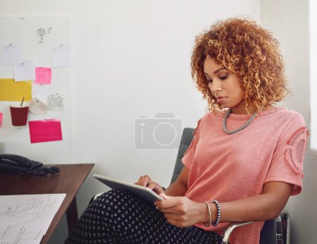 Foto de Se toma en serio el diseño. una joven diseñadora enfocada usando su tableta mientras está sentada en un escritorio en la oficina - Imagen libre de derechos