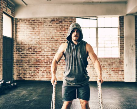 Photo for Doing it right while looking like a pro. a hooded and determined young man making use of ropes to workout in the gym - Royalty Free Image