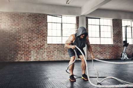 Photo for Im going to conquer and crush my goals. a muscular young man working out with battle ropes in a gym - Royalty Free Image