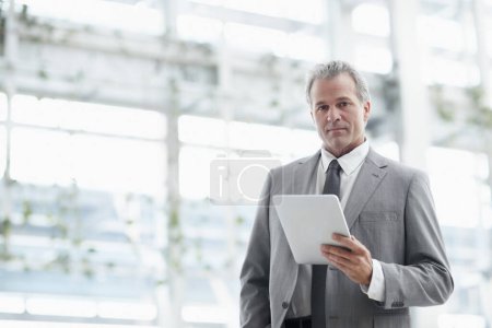Foto de La tecnología ha revolucionado mi negocio. Retrato de un hombre de negocios maduro usando una tableta digital mientras está de pie en la oficina - Imagen libre de derechos